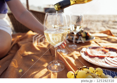 Close-up of a glass of champagne on a picnic mat. The cup is filled with sparkling wine outdoors on the beach. Delicious snacks and drinks by the sea. 125192310