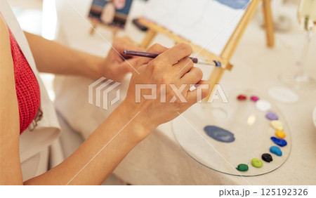 Close-up of woman hands and a palette with paints. The artist holds a brush and mixes acrylic paints 125192326