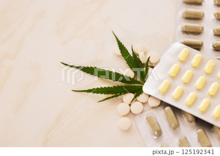 Mockups of medicines on a beige background with cannabis leaf. Close up of blisters with pills on a marble table with green hemp. Mockups of medicines on a beige background with cannabis leaf. Close up of blisters with pills on a marble table with green hemp. 125192341