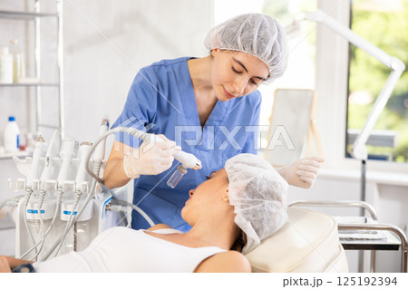 Female aesthetician applying atomized nutrients onto woman client face 125192394