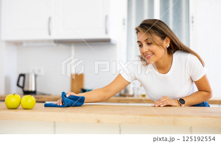 Cheerful young Latina cleaning table in kitchen at home 125192554