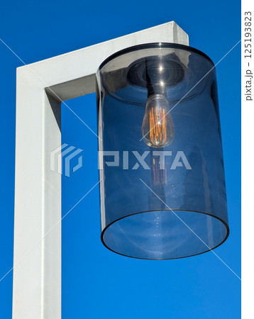 Modern lamp with glass shade against clear blue sky. 125193823