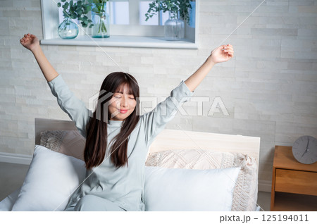 ベッドで伸びをする若い女性 125194011