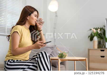 Morning Refreshment and Healthy Choices. A woman sipping water while enjoying a salad during her morning routine. Morning Refreshment and Healthy Choices. A woman sipping water while enjoying a salad during her morning routine. 125194276