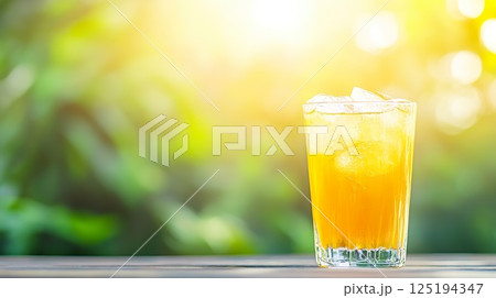 Refreshing glass of iced orange juice in sunlit garden setting. 125194347