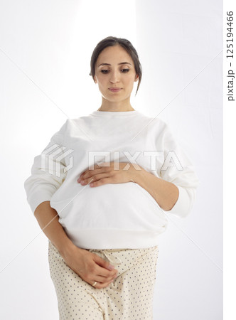 A stylish pregnant woman gently holds onto her belly. The expectant mother touches her tummy 125194466