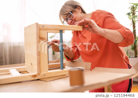 An elderly woman in orange casual clothes is painting a wooden chair in the living room An elderly woman in orange casual clothes is painting a wooden chair in the living room 125194468