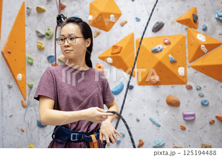 A young Asian woman on a climbing wall. A Korean girl climbs a bouldering wall 125194488