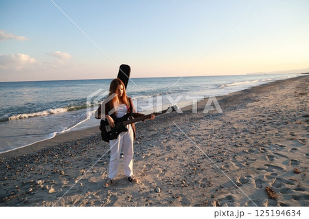 Girl Walks And Plays The Bass Instrument On The Beach Near The Ocean At Sunset Girl Walks And Plays The Bass Instrument On The Beach Near The Ocean At Sunset 125194634