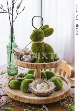 Green moss Easter Bunny and decorative Easter eggs in nest on on two tiered wooden plate 125195542