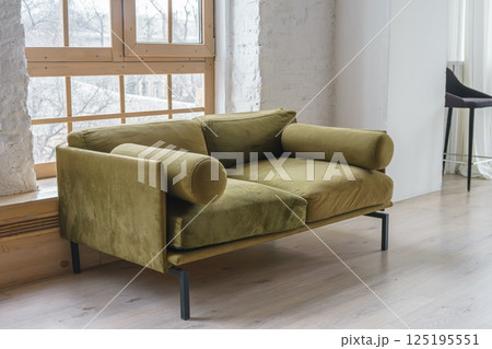 Cozy green khaki couch in bright and airy living space with large windows and brick wall backround Cozy green khaki couch in bright and airy living space with large windows and brick wall backround 125195551
