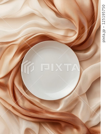 White plate on flowing beige fabric 125195750