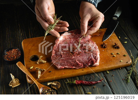 Hands skillfully season a raw cut of meat with an array of spices and fresh herbs on a wooden cutting board, showcasing culinary expertise in a cozy kitchen environment Hands skillfully season a raw cut of meat with an array of spices and fresh herbs on a wooden cutting board, showcasing culinary expertise in a cozy kitchen environment 125196019