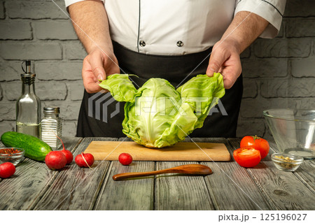 A chef is showcasing a fresh cabbage in a cozy kitchen, surrounded by various vegetables like radishes, tomatoes, and cucumbers, preparing for a meal A chef is showcasing a fresh cabbage in a cozy kitchen, surrounded by various vegetables like radishes, tomatoes, and cucumbers, preparing for a meal 125196027