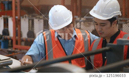 Engineer teaching apprentice to use metal sheet stamping machine, industrial team is working on various projects with tablet computer, worker work together to check the operation system in a factory 125196033