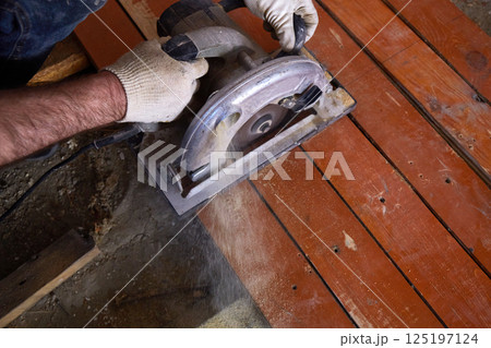 Craftsman operates a circular saw to cut through wooden planks in a well-lit workshop. Craftsman operates a circular saw to cut through wooden planks in a well-lit workshop. 125197124