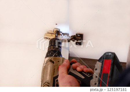 Installing a furniture hinge on a door, assembling furniture and fastening fittings. Installing a furniture hinge on a door, assembling furniture and fastening fittings. 125197181