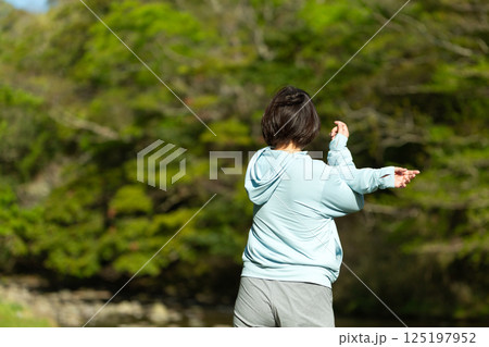 新緑の川辺で体操をするミドル女性 125197952