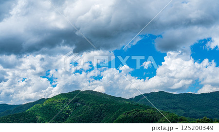 夏の青空に流れるたくさんの白い雲と、新緑の山並み 125200349