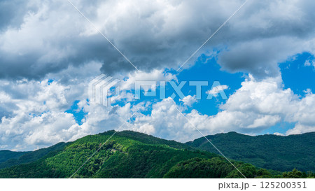 夏の青空に流れるたくさんの白い雲と、新緑の山並み 125200351