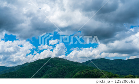 夏の青空に流れるたくさんの白い雲と、新緑の山並み 夏の青空に流れるたくさんの白い雲と、新緑の山並み 125200365