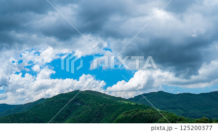 夏の青空に流れるたくさんの白い雲と、新緑の山並み 夏の青空に流れるたくさんの白い雲と、新緑の山並み 125200377