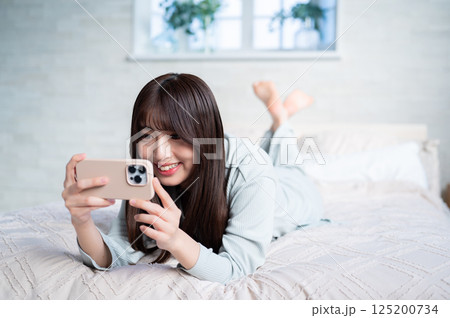 うつ伏せでスマホを持つ若い女性 うつ伏せでスマホを持つ若い女性 125200734
