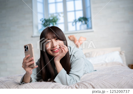うつ伏せでスマホを持つ若い女性 うつ伏せでスマホを持つ若い女性 125200737