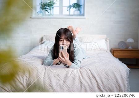 うつ伏せでスマホを持つ若い女性 うつ伏せでスマホを持つ若い女性 125200740