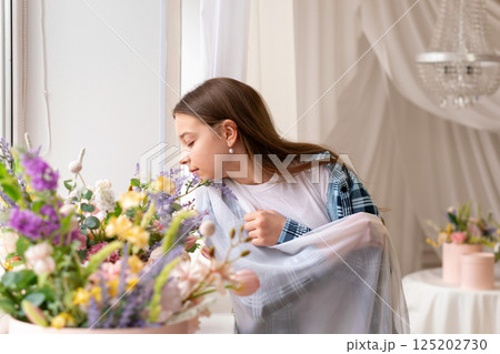 Girl smelling flowers near window with closed eyes indoors. 125202730