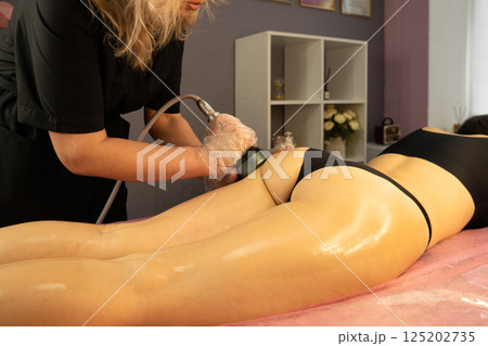 Beautician performs radiofrequency treatment on client's gluteal area. Beautician performs radiofrequency treatment on client's gluteal area. 125202735