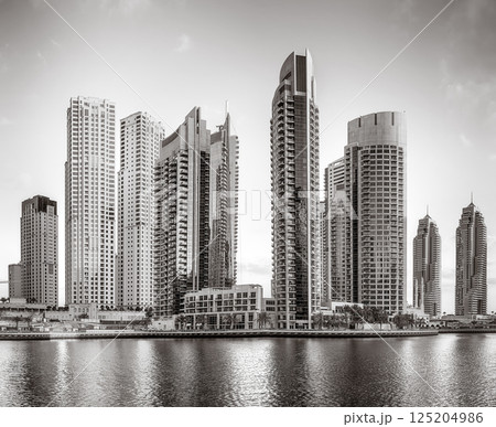 Monochrome city skyline with tall skyscrapers reflecting on calm water under a cloudy sky, Dubai Marina bay UAE Monochrome city skyline with tall skyscrapers reflecting on calm water under a cloudy sky, Dubai Marina bay UAE 125204986