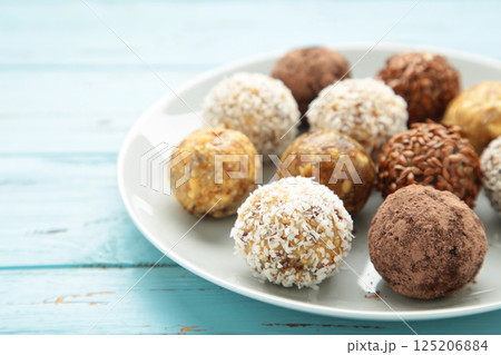 Healthy raw energy balls. Candy vegan balls of dates, nuts and coconut on plate on blue background. Top view, concept of useful home-made candies without sugar Healthy raw energy balls. Candy vegan balls of dates, nuts and coconut on plate on blue background. Top view, concept of useful home-made candies without sugar 125206884