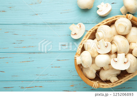 Fresh white champignon mushrooms on basket on blue wooden background. 125206893