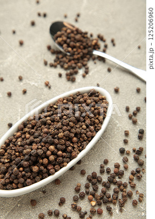 Black pepper corns in white plate on grey concrete background. Vertical photo 125206960