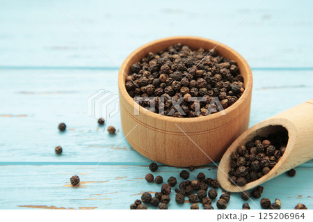 Black peppercorns in wooden bowl and spoon on blue wooden background. 125206964