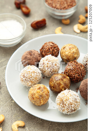Healthy raw energy balls. Candy vegan balls of dates, nuts and coconut on light background. Top view, concept of useful home-made candies without sugar. Vertical photo Healthy raw energy balls. Candy vegan balls of dates, nuts and coconut on light background. Top view, concept of useful home-made candies without sugar. Vertical photo 125207009