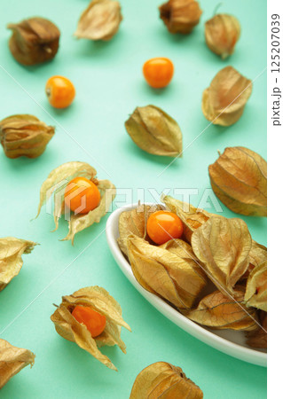 Physalis peruviana fruit on white plate on mint background. Vertical photo 125207039