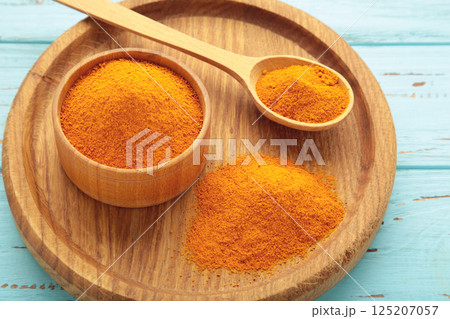 Turmeric (Curcuma) powder on wooden plate on blue background Turmeric (Curcuma) powder on wooden plate on blue background 125207057