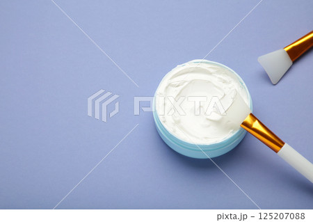 Cosmetic mask (scrub) in a bowl with brush on purple background. 125207088