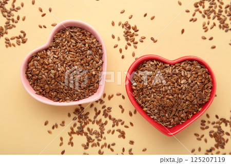 Healthy food. Flax seeds in pink and red heart shaped bowls on beige background. 125207119