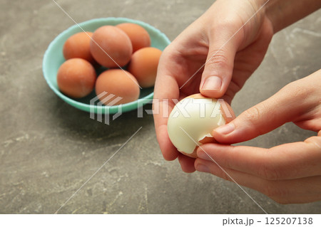 Woman peeling boiled egg on grey background, closeup Woman peeling boiled egg on grey background, closeup 125207138