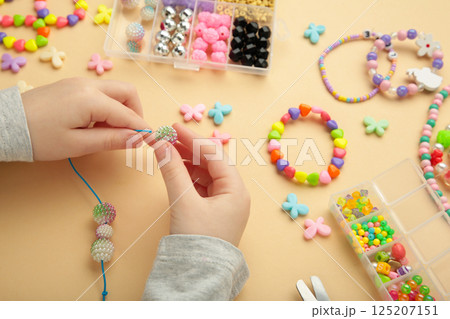 Little girl made bracelets on beige background. Kids handmade beaded jewelry. DIY bracelet beads. Little girl made bracelets on beige background. Kids handmade beaded jewelry. DIY bracelet beads. 125207151