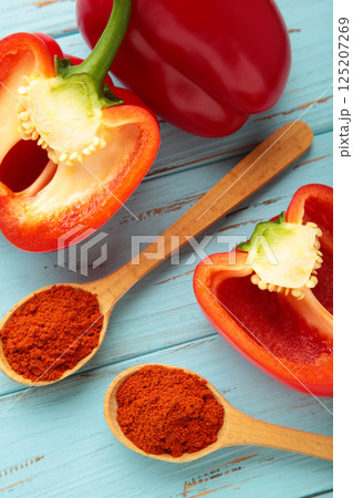 Powder paprika on wooden spoon with fresh red pepper on blue wooden background. Vertical photo 125207269
