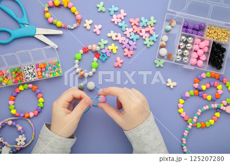 Little girl made bracelets on purple background. Kids handmade beaded jewelry. DIY bracelet beads. 125207280