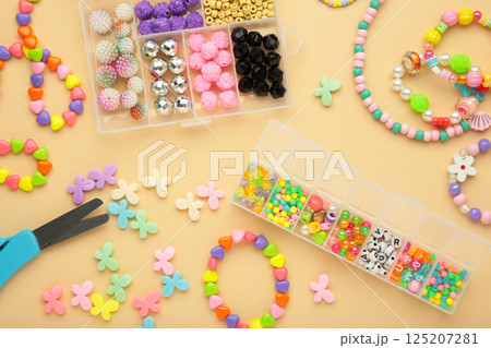 Box with beads to create hand made jewelry for child on beige background. Making bracelet. Handmade accessories. 125207281