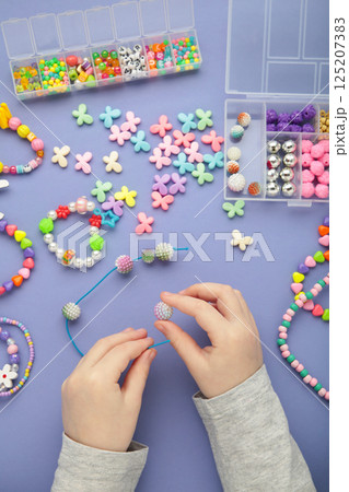 Little girl made bracelets on violet background. Kids handmade beaded jewelry. DIY bracelet beads. Little girl made bracelets on violet background. Kids handmade beaded jewelry. DIY bracelet beads. 125207383