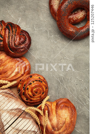 Bakery - various kinds of breadstuff. Bread rolls, bagel, sweet bun on grey background. Vertical photo 125207446