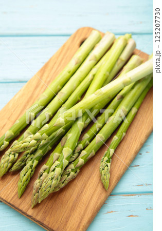 Fresh green asparagus on cutting board on blue wooden background. Healthy food concept. Fresh green asparagus on cutting board on blue wooden background. Healthy food concept. 125207730