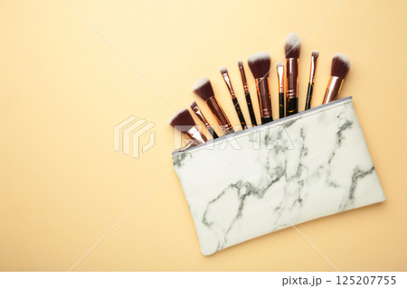 Cosmetic bag with different brushes of professional makeup artist on beige background 125207755